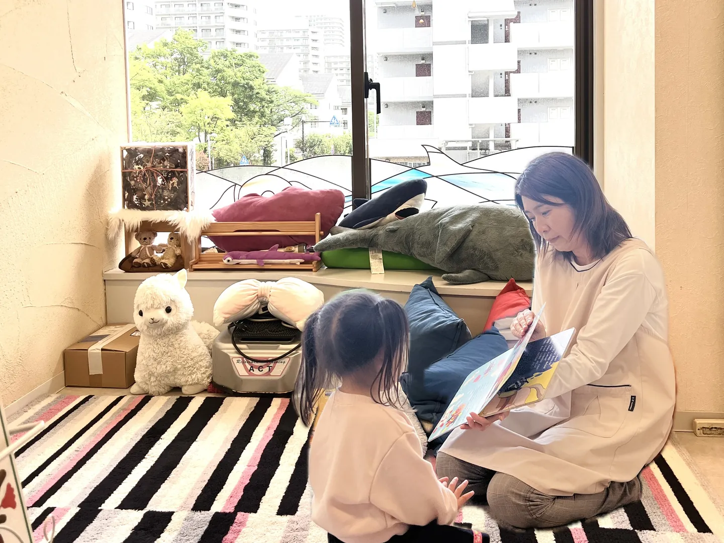 キッズルームで保育士と絵本を読む子ども